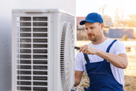 HVAC technician in blue workwear servicing an outdoor condenser